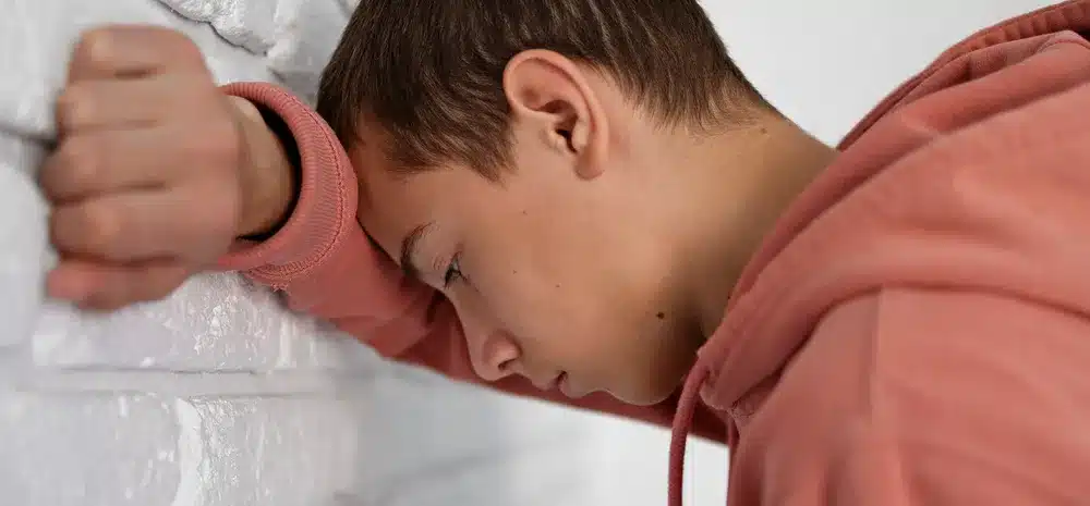 adolescente triste apoyado pared min