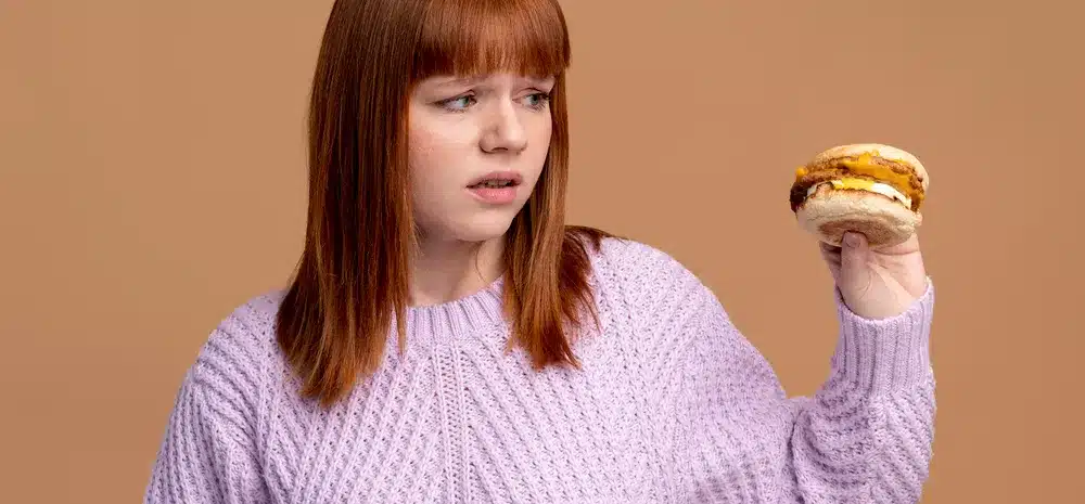 mujer con trastorno alimentario intentando comer hamburguesa min