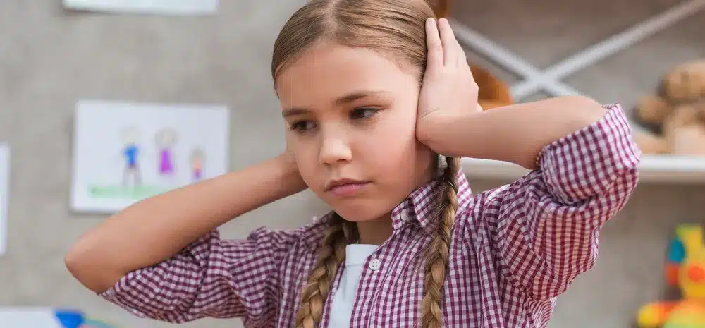 nina triste tapando sus oidos con dos manos min